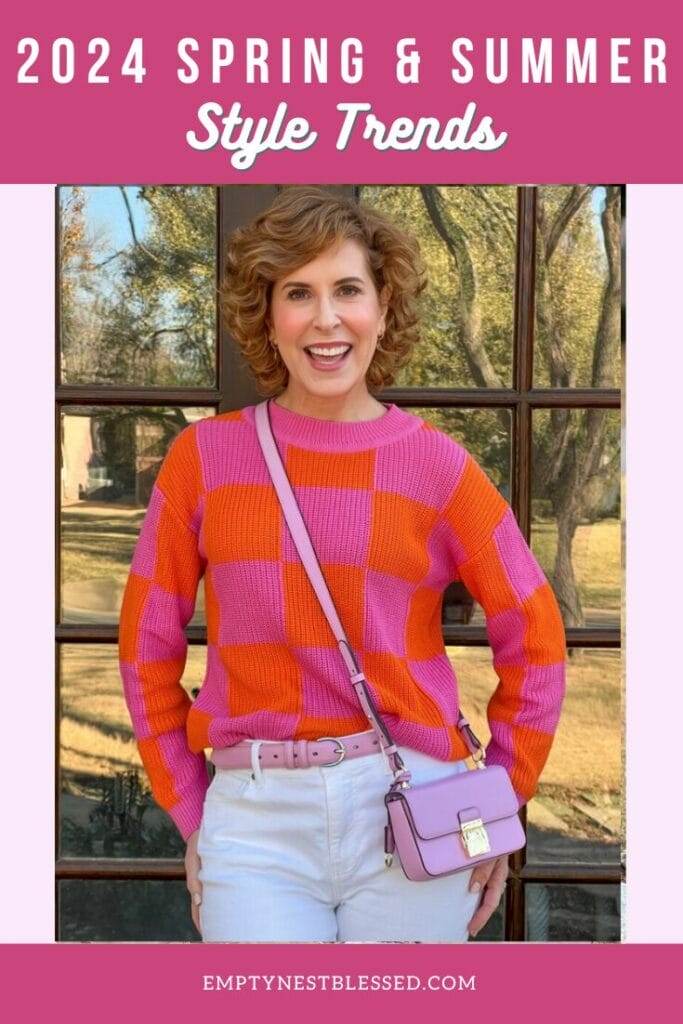 pinterest pin of woman over 50 wearing pink and orange sweater from avara standing in front of french doors photographed waist up