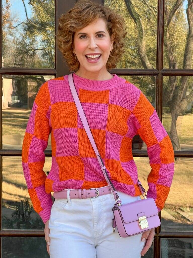 woman over 50 wearing pink and orange sweater from avara standing in front of french doors photographed waist up