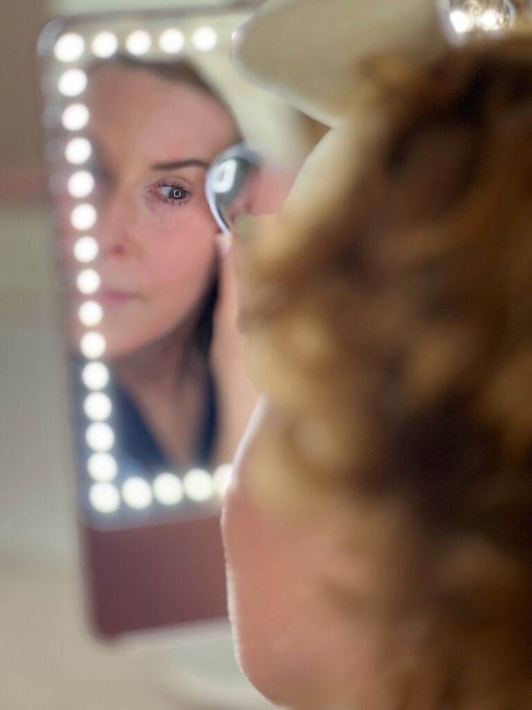 woman over 50 with her hair in a bow headband and wearing a robe using Ziip Halo microcurrent and nanocurrent device while looking into a mirror