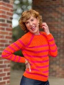 woman touching hair wearing orange and pink stripe sweater