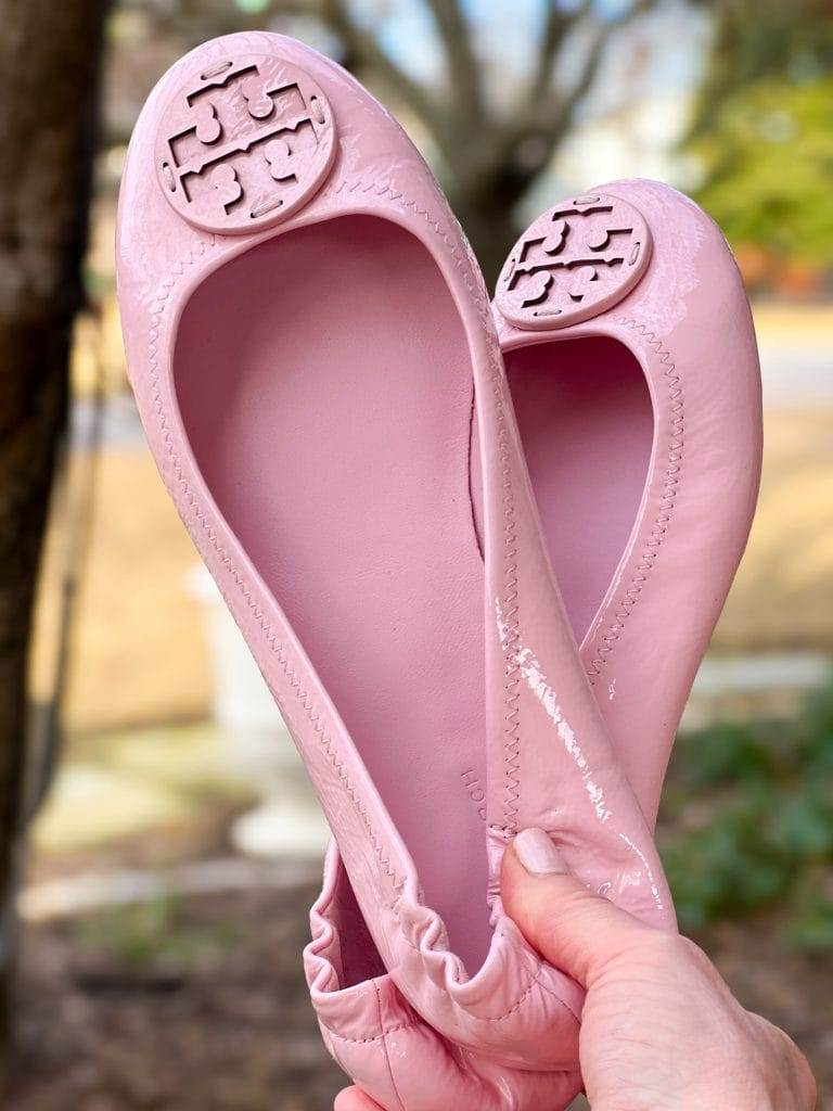 woman's hand holding up tory burch pink ballet flats