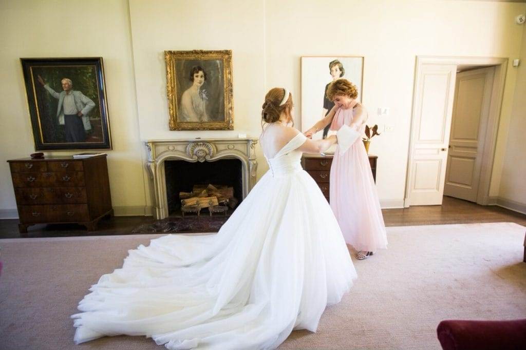 woman in blush dress holding hands with bride and looking at her dress.