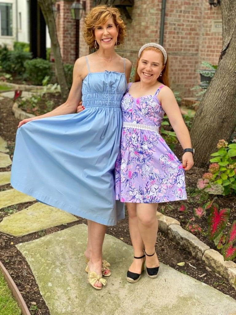 Woman over 50 in blue dress and young girl with red hair in purple dress posing outside