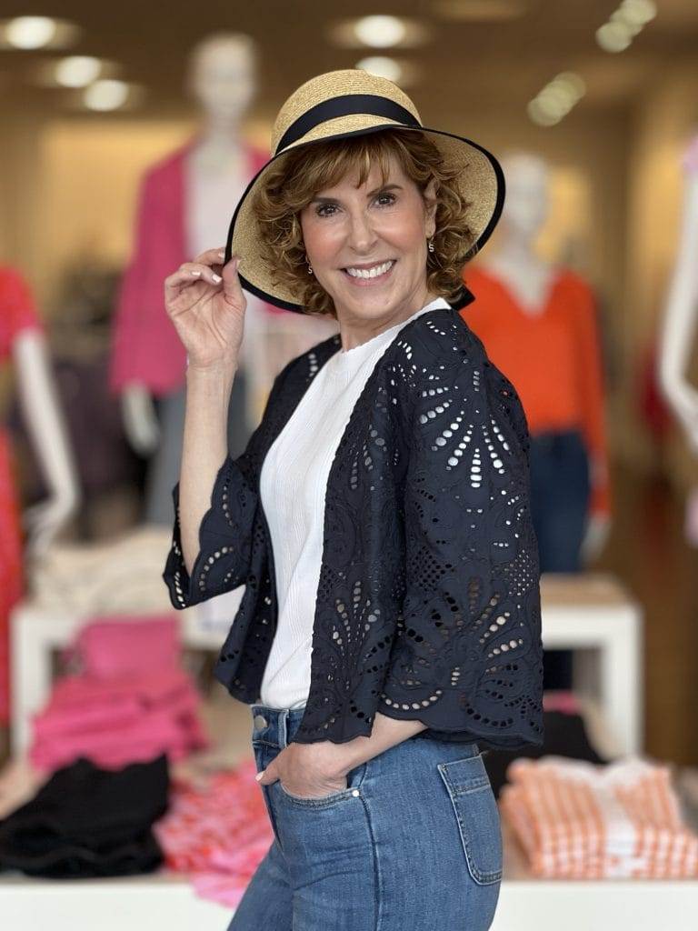 woman dressed in white tee and crochet navy 3/4 sleeve jacket wearing straw hat