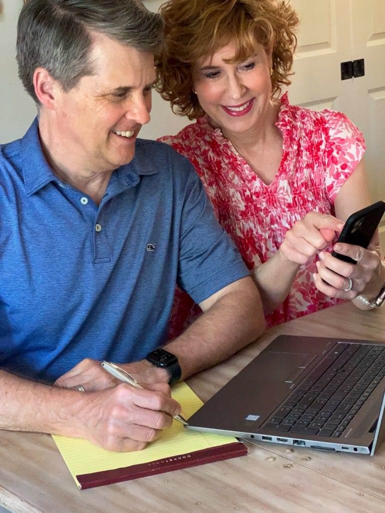 husband and wife sitting at a table looking at a computer and an iphone