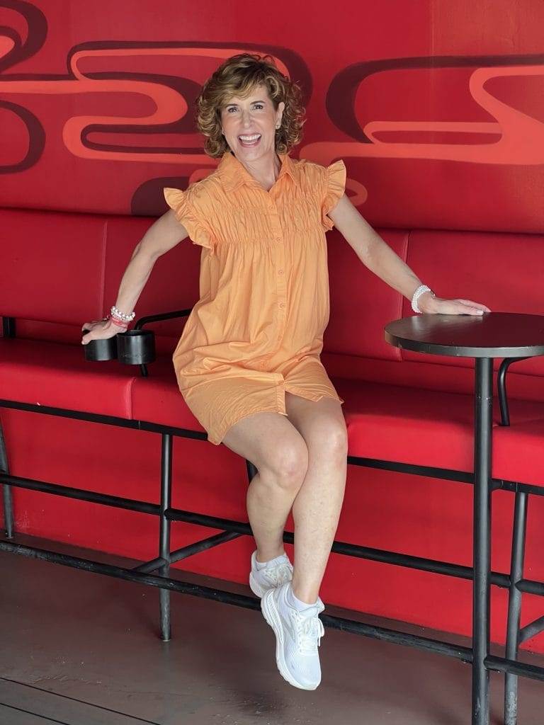 woman sitting on red bench on cruise ship wearing orange neacie dress from avara