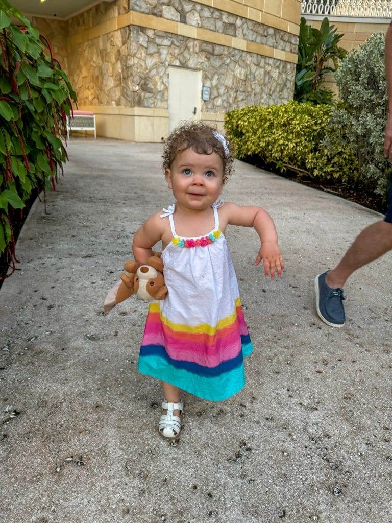 18 month old baby with curly hair wearing hatley girl dress with pom poms at baha mar