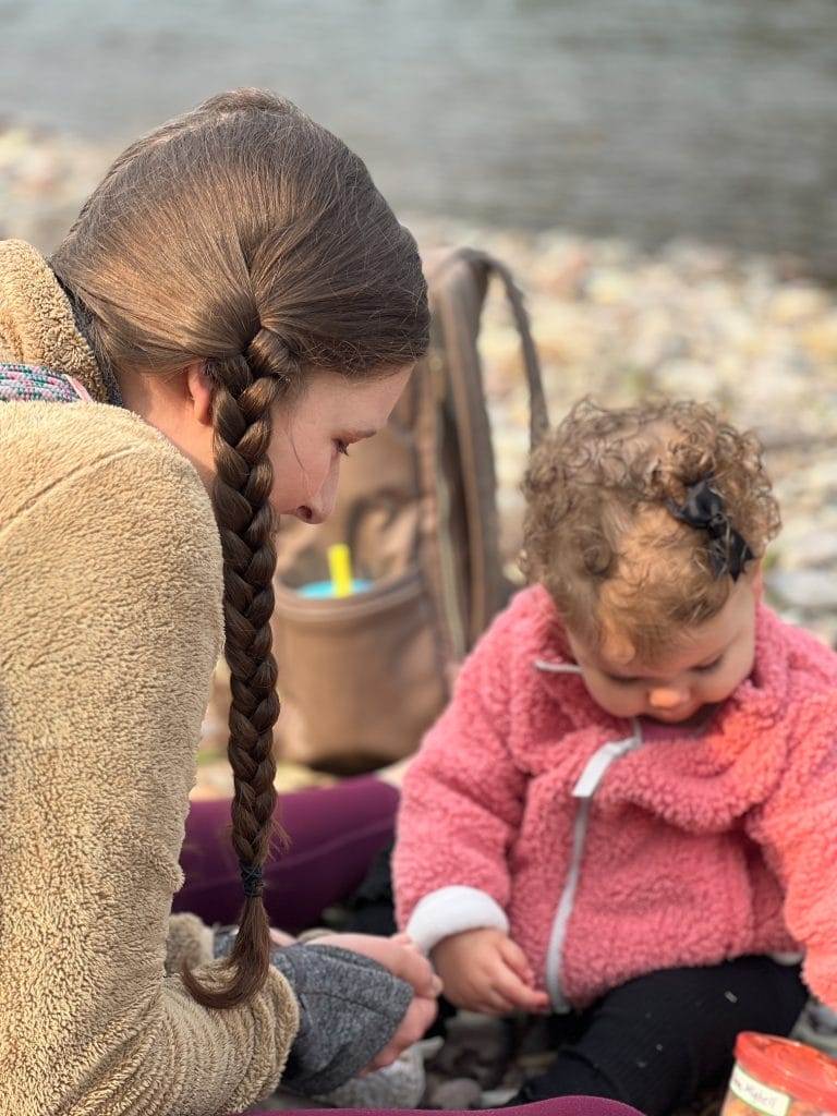 girl in braids and baby in pink jacket near a river