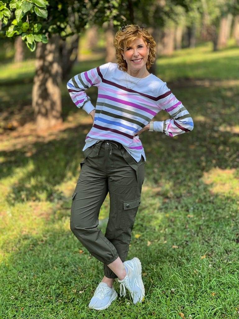 woman over 50 standing in the woods wearing a transitional outfit