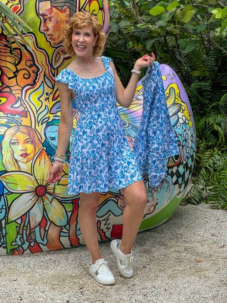 woman wearing lilly pulitzer Jilly Smocked Dress and holding Sea View Linen Button Down Top | Lilly Pulitzer in front of a colorful grafitti rock