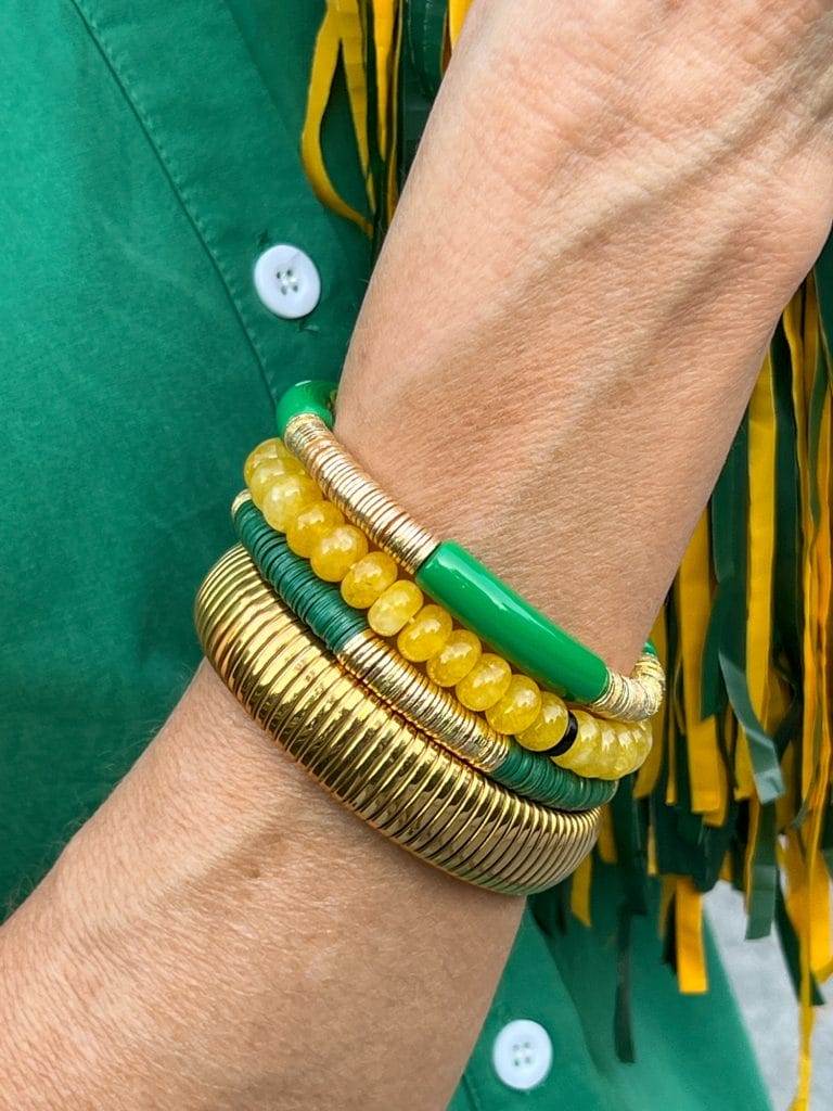 picture of women's wrist with a stack of braclets in yellow, gold, and green