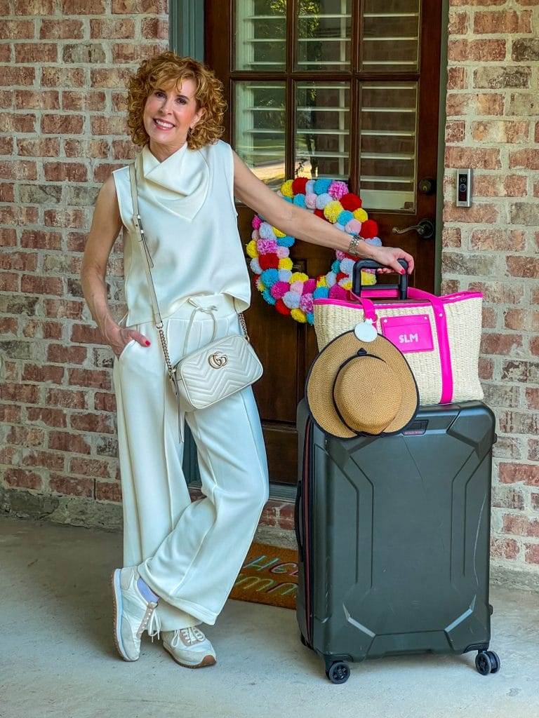 woman getting ready for travel to baha mar wearing talbots ivory airknit travel pieces and standing by luggage