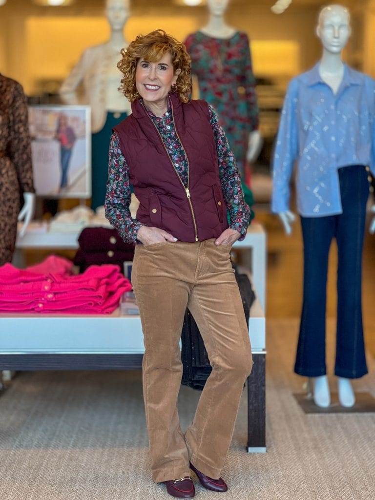 woman over 50 standing in a talbots store wearing tan cords, a print shirt and a wine vest