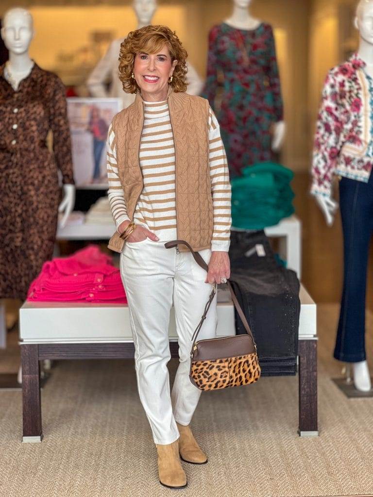 woman over 50 standing in a talbots store wearing striped top, tan sweater vest, and ivory pants