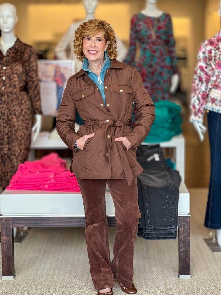 woman over 50 wearing brown coat and pants with teal sweater underneath standing in Talbots store