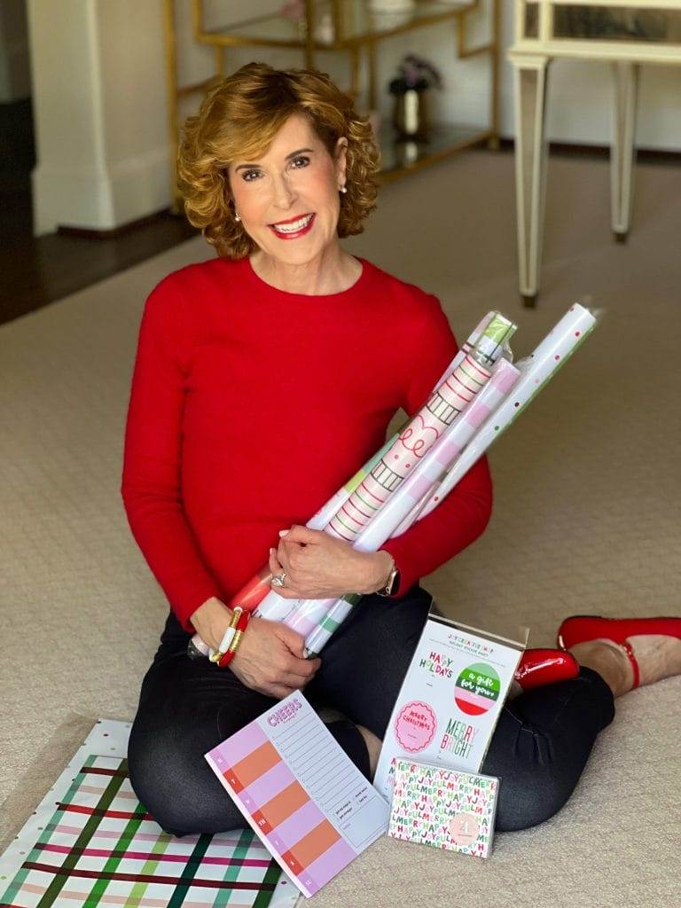 Woman in red shirt and black pants sitting on the floor holding christmas wrapping paper and stickers