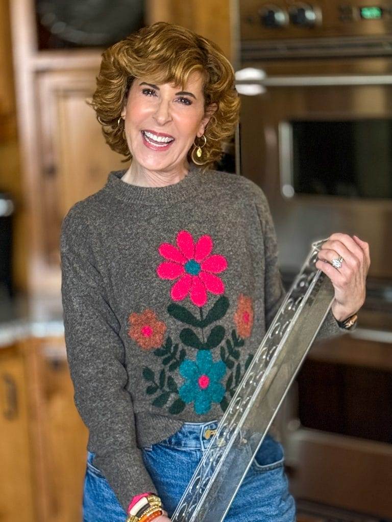 Woman standing in a kitchen with a brown floral sweater holding an acrylic rectangle flower vase