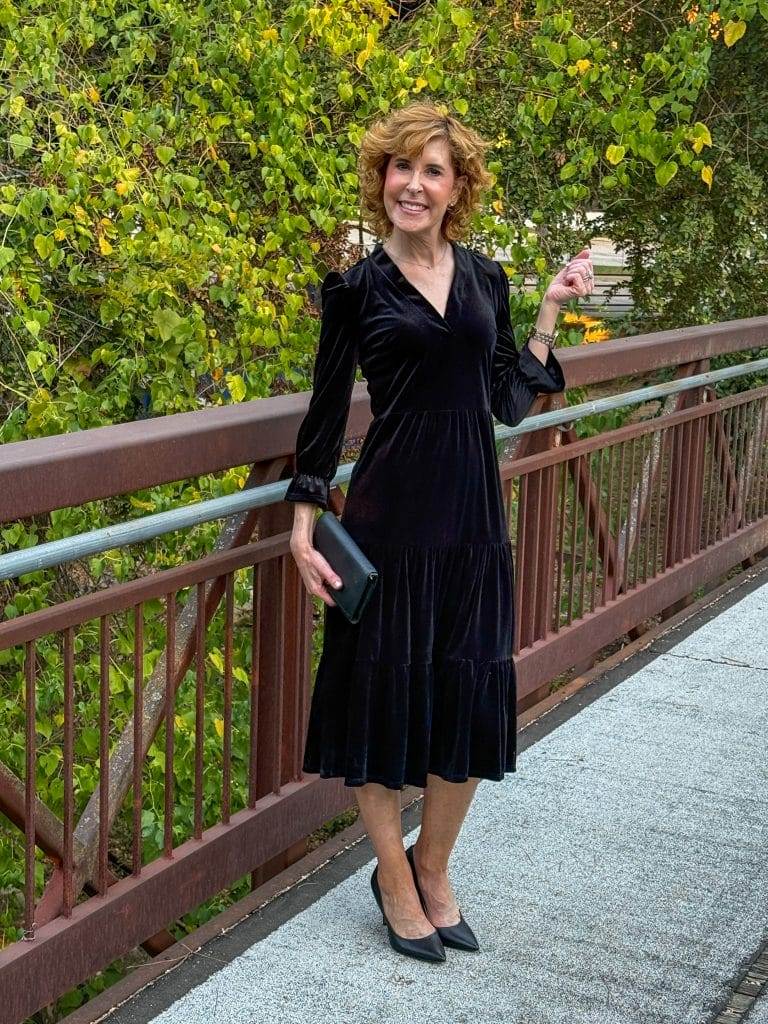 woman standing on bridge wearing black velvet midi dress