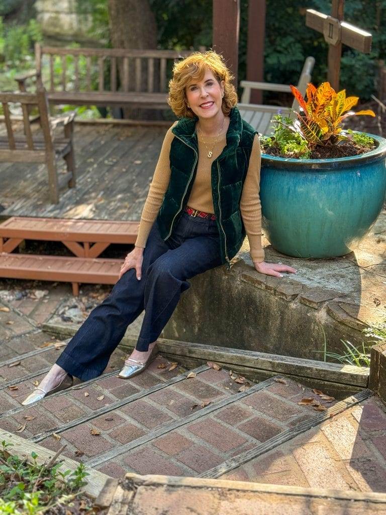 woman sitting on a stone wall wearing talbots velvet puffer vest and jeans with gold metallic sweater underneath