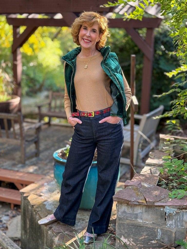 woman standing outdoors wearing green velvet puffer, gold metallic shirt, and jeans