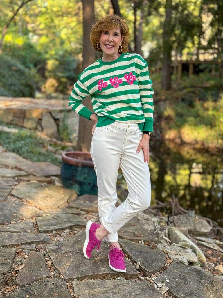 woman wearing avara falala  sweatshirt and white jeans standing in the woods