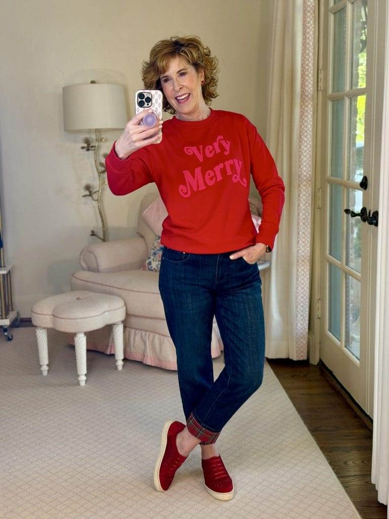 woman over 50 taking a selfie wearing a red very merry sweatshirt and jeans with a steward plaid hem and red sneakers