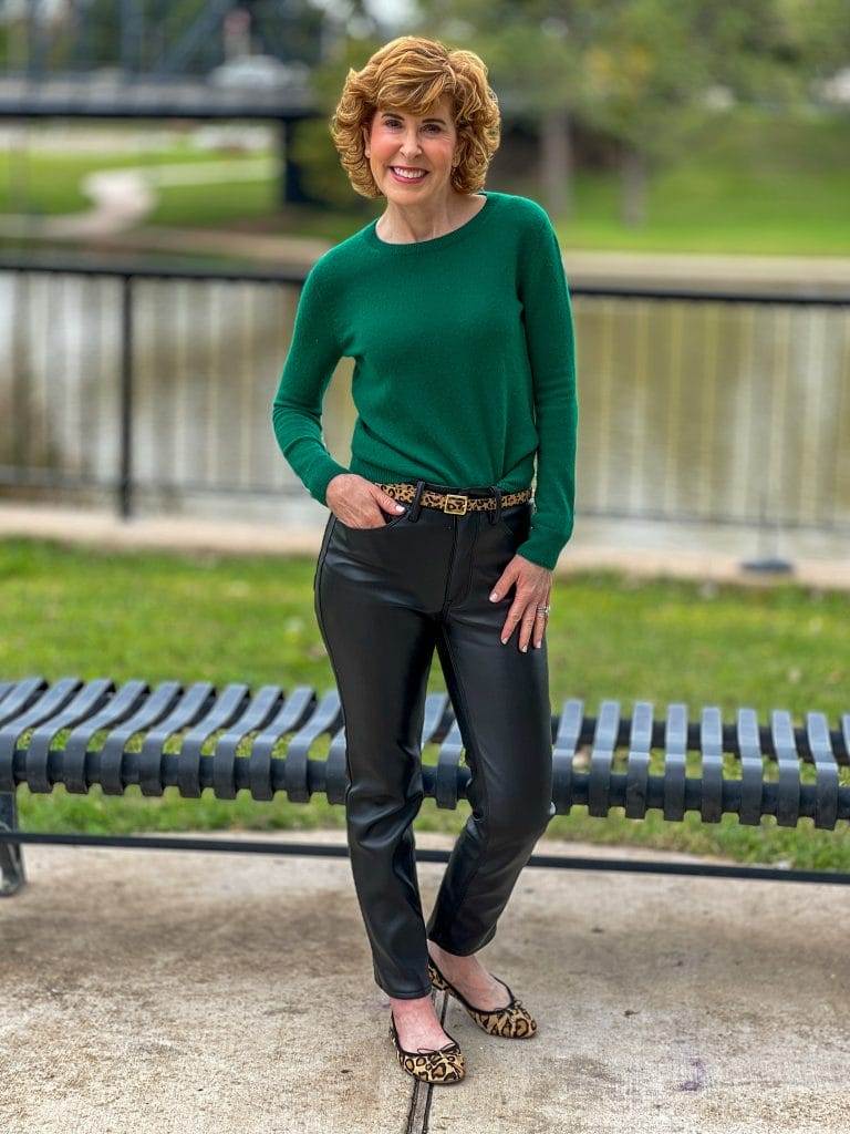 woman over 50 standing by the side of the brazos river    wearing green cashmere sweater and faux leather jean