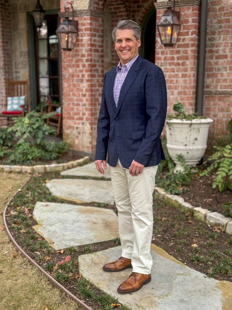 man standing on pavers in front yard wearing khakis, a shirt, and a blazer