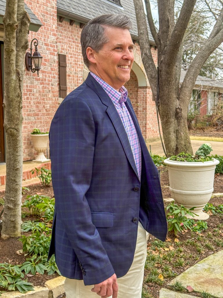 Man standing in yard looking away from the camera wearing shirt and blazer