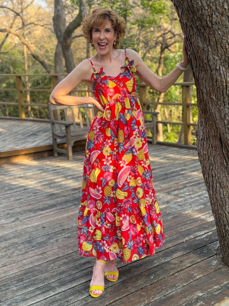 Woman standing on a wooden deck by a tree wearing a red fruit motif dress