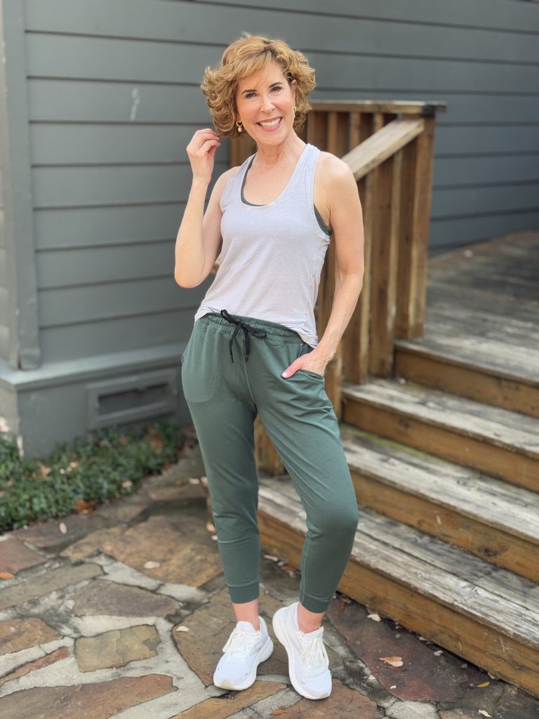 woman over 50 wearing definite articles sports bra, tank top, and joggers standing on a stone walkway by a stream