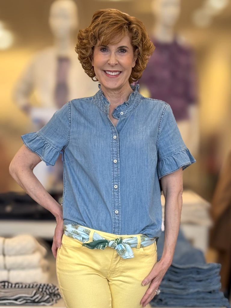 woman over 50 standing and modeling a ruffle sleeve chambray top