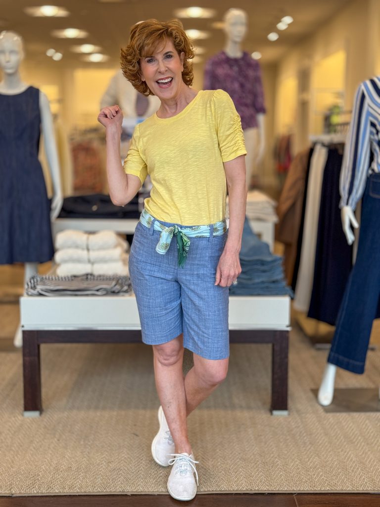 woman over 50 posing in a store wearing yellow elbow length tee and chambray shorts