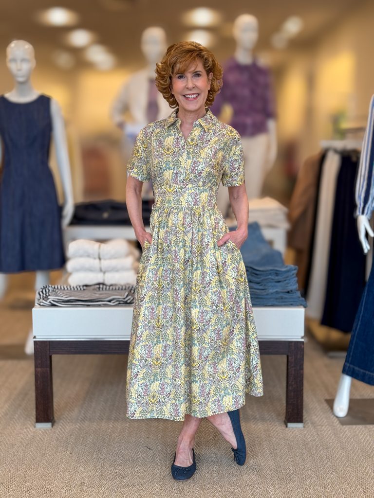 woman over 50 posing in a store wearing a yellow print shirtdress