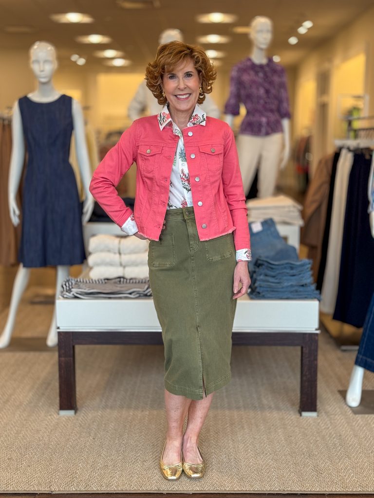 woman over 50 posing in a store wearing coral denim jacket and army green straight skirt