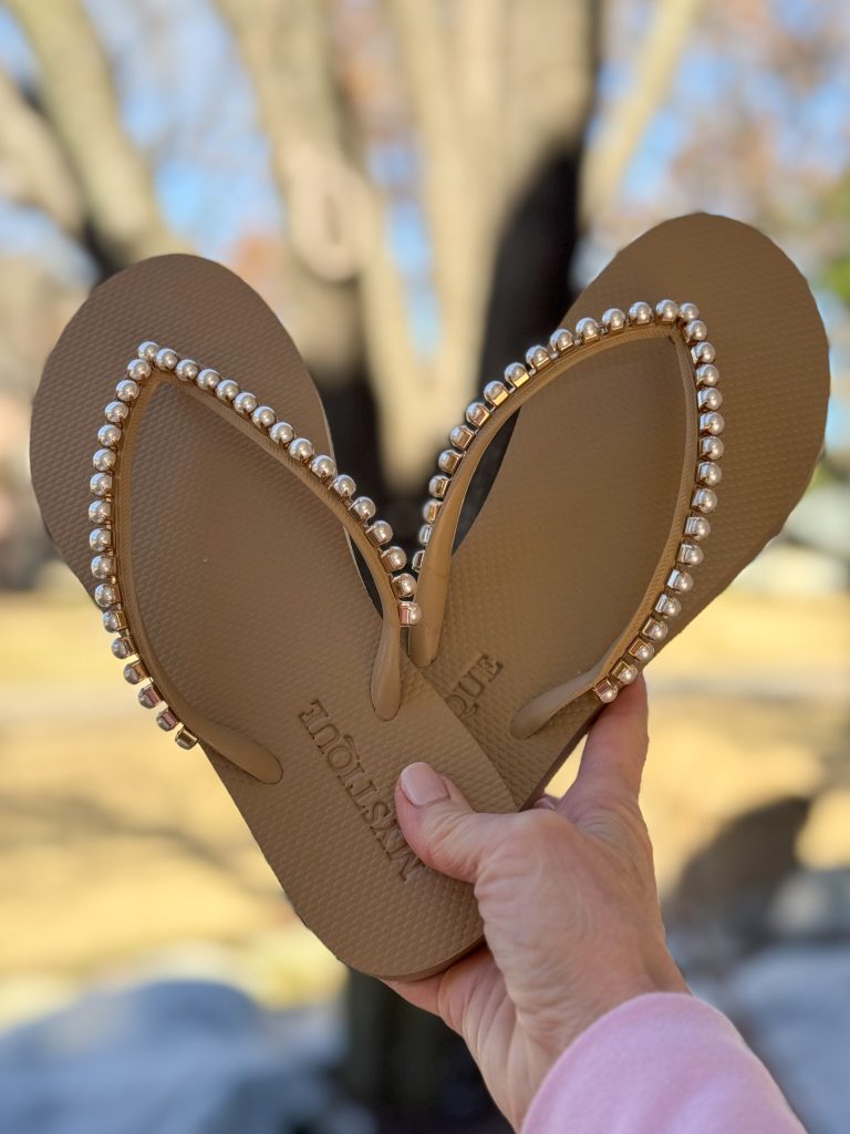 womans hand holding a pair of mystique Outingdale Flip Flops with pearl embellishments