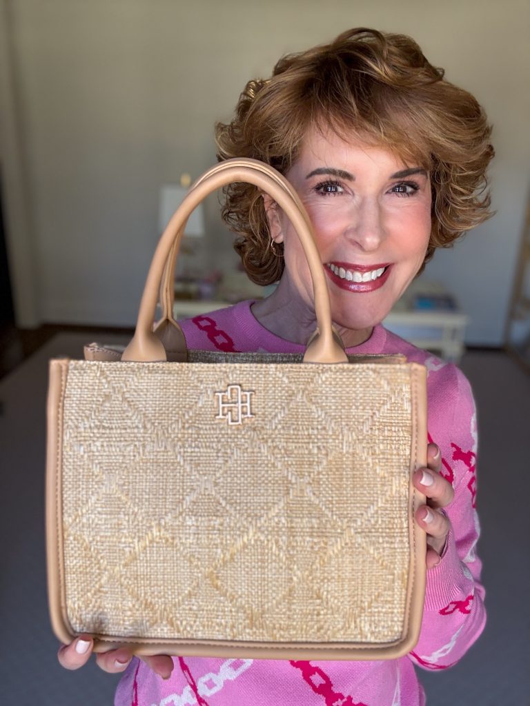 woman wearing pink sweater holding a straw top handle bag