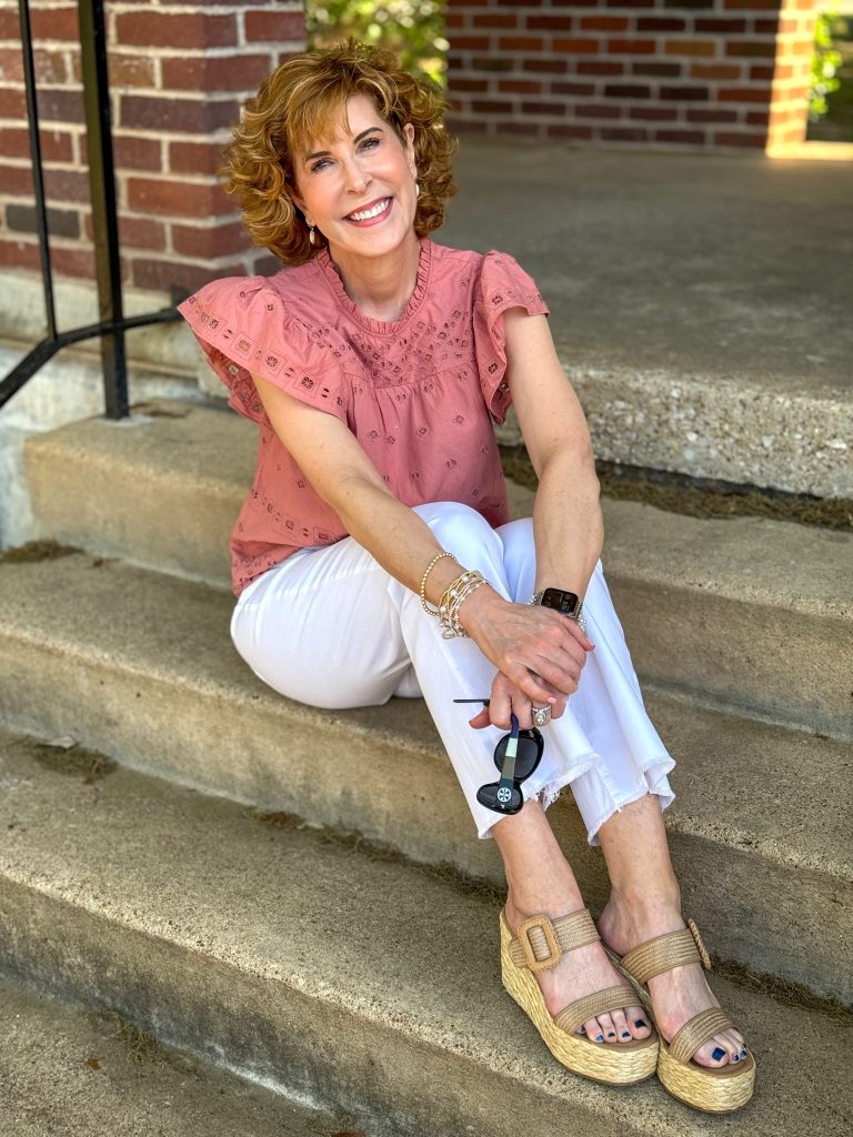 woman over 50 sitting on outdoor stairs wearing lands' end coral eyelet top and white jeans