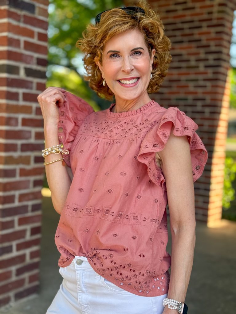 woman over 50 looking into camera and touching the sleeve of her eyelet shirt
