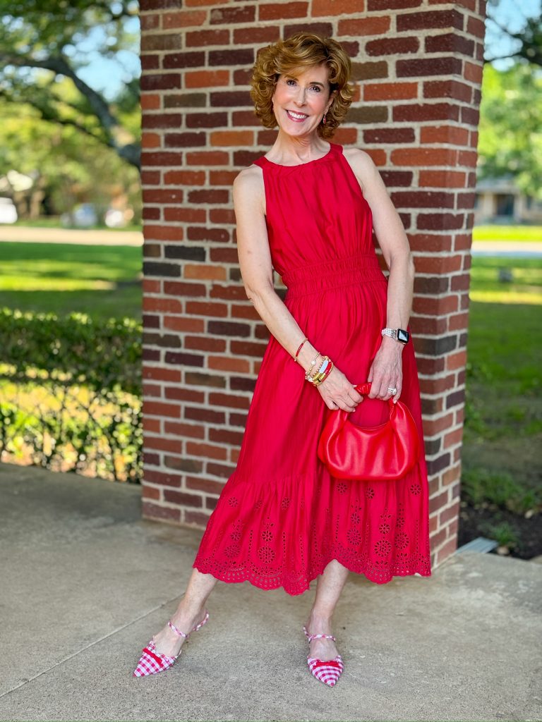 woman standing outside in front of a brick wall in red halter dress holding red handbag and wearing red and white gingham kitten heels