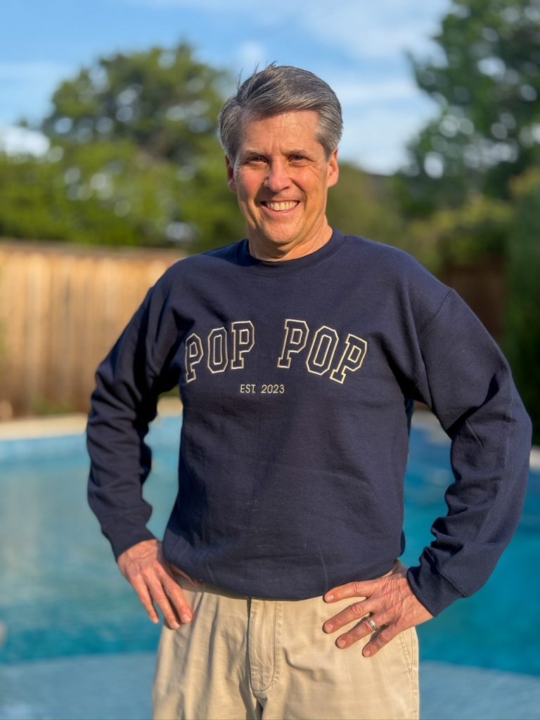 man standing next to a pool with a monogrammed navy blue sweathsirt that says pop pop on it
