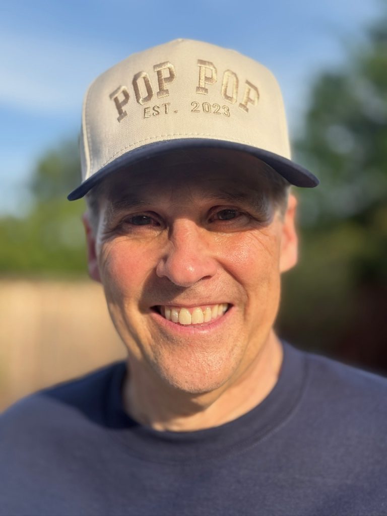 man standing outside with monogrammed baseball hat that says pop pop on it