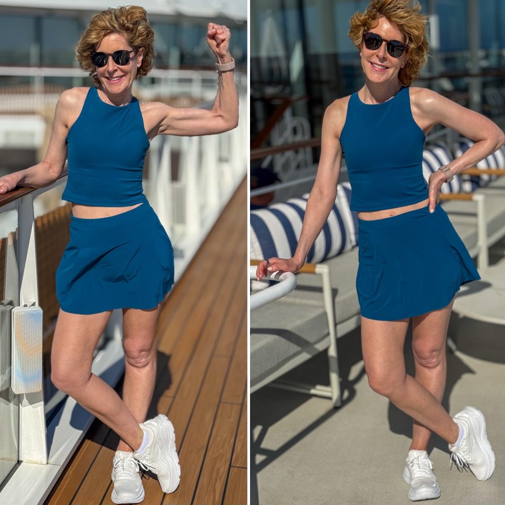 Woman on cruise ship deck wearing a teal athletic two-piece set with a sleeveless crop top and skort, styled with white sneakers and sunglasses, posing in bright sunlight.